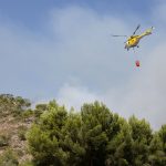 Helicóptero lança água sobre uma área de floresta em chamas na Espanha durante o combate a um incêndio florestal.