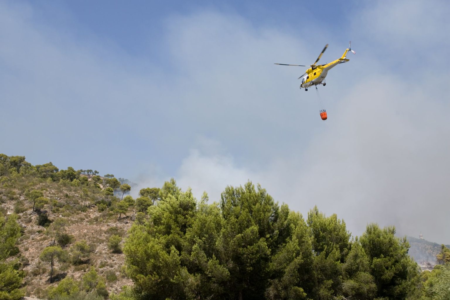 Helicóptero lança água sobre uma área de floresta em chamas na Espanha durante o combate a um incêndio florestal.