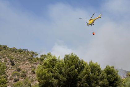 Helicóptero lança água sobre uma área de floresta em chamas na Espanha durante o combate a um incêndio florestal.