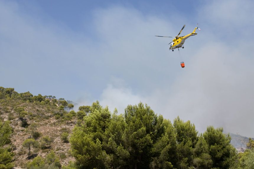 Helicóptero lança água sobre uma área de floresta em chamas na Espanha durante o combate a um incêndio florestal.