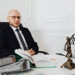 Advogado analisa documentos jurídicos em um escritório, ao lado de uma estátua da Justiça.