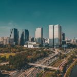 Vista aérea do horizonte de São Paulo, com edifícios modernos e uma via expressa em primeiro plano.