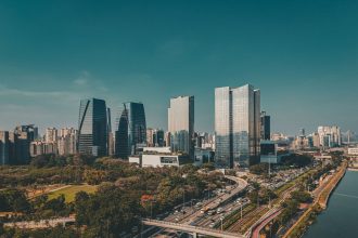Vista aérea do horizonte de São Paulo, com edifícios modernos e uma via expressa em primeiro plano.