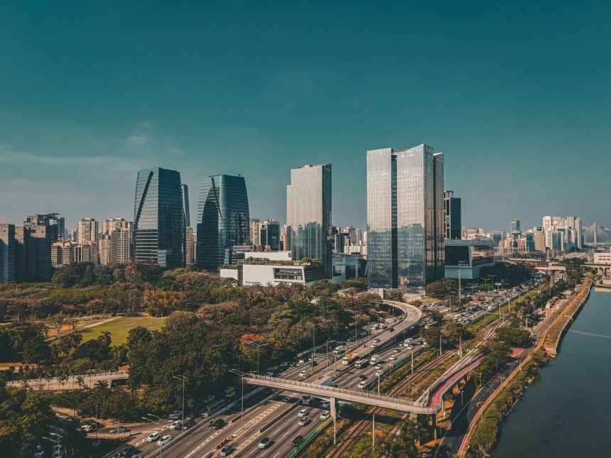 Vista aérea do horizonte de São Paulo, com edifícios modernos e uma via expressa em primeiro plano.